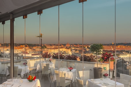 A rooftop restaurant with tables set for dining, overlooking a cityscape.