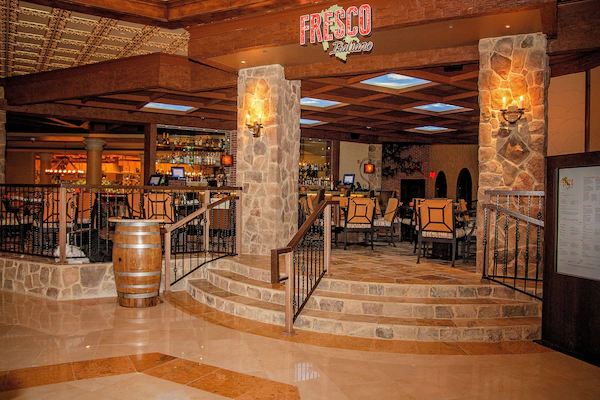 A bar area with stone pillars, wooden bar stools, and a wooden barrel.