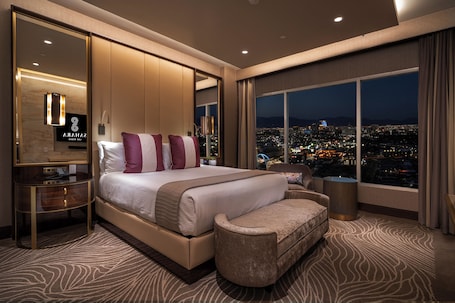 A modern hotel room with a large bed, a seating area, and a city view.