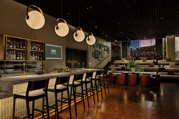 A bar area with a long counter, multiple stools, and a variety of bottles and glasses on shelves.