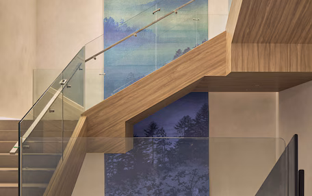 A modern interior with a wooden staircase, glass railings, and a large mural of a forest scene.