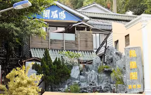 A traditional Japanese building with a blue sign, wooden exterior, and a rock garden in front.