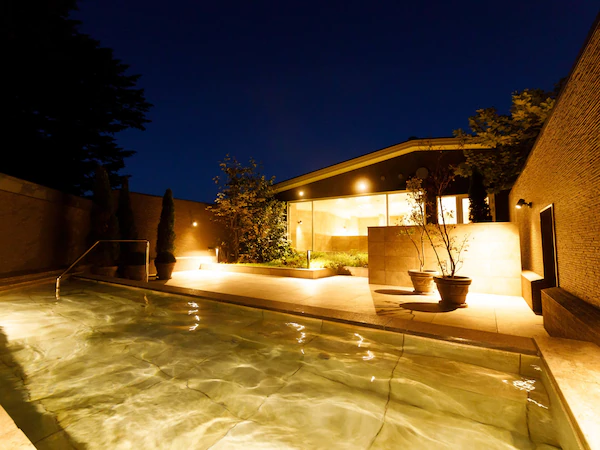 A swimming pool with clear water, surrounded by a brick wall and potted plants.