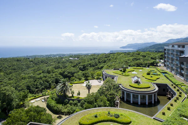 An aerial view of a hotel with a landscaped garden, a circular building, and a view of the sea.