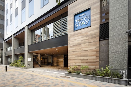 A hotel entrance with a brick facade, outdoor seating area, and potted plants.