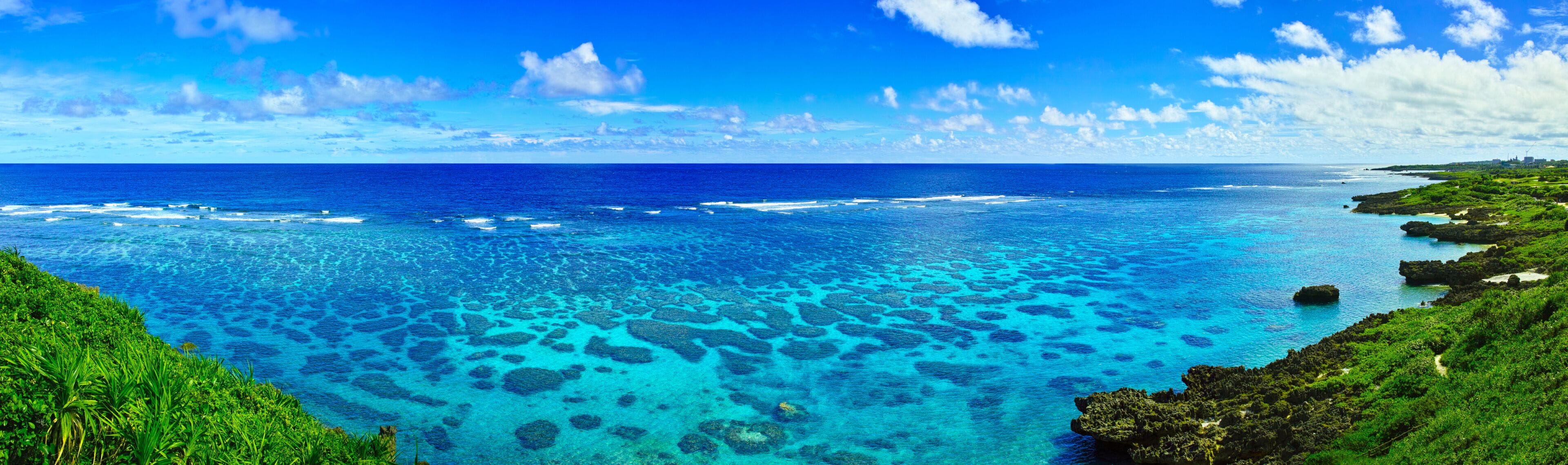 A coastal landscape with clear blue waters, visible coral reefs, and lush greenery.