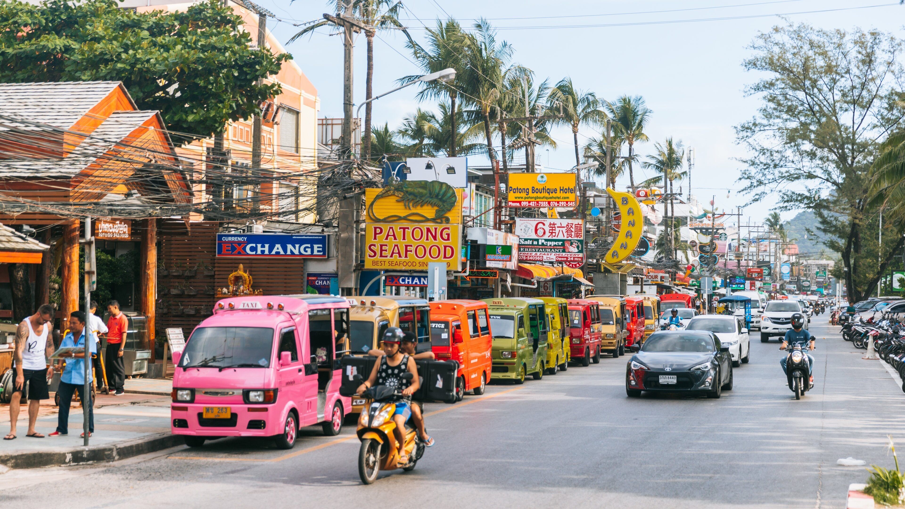 A busy street with colorful food trucks, a pink taxi, and motorcycles.